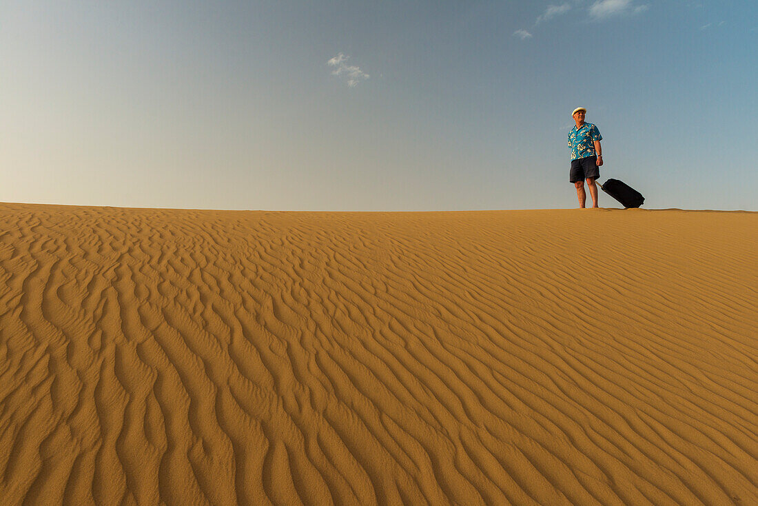 Barfüßiger Mann mit Koffer auf Sanddüne,Dubai,Vereinigte Arabische Emirate