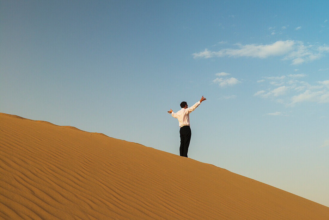 Man In Smart Clothes Waving For Attention On Top Of Sand Dune,Dubai,United Arab Emirates