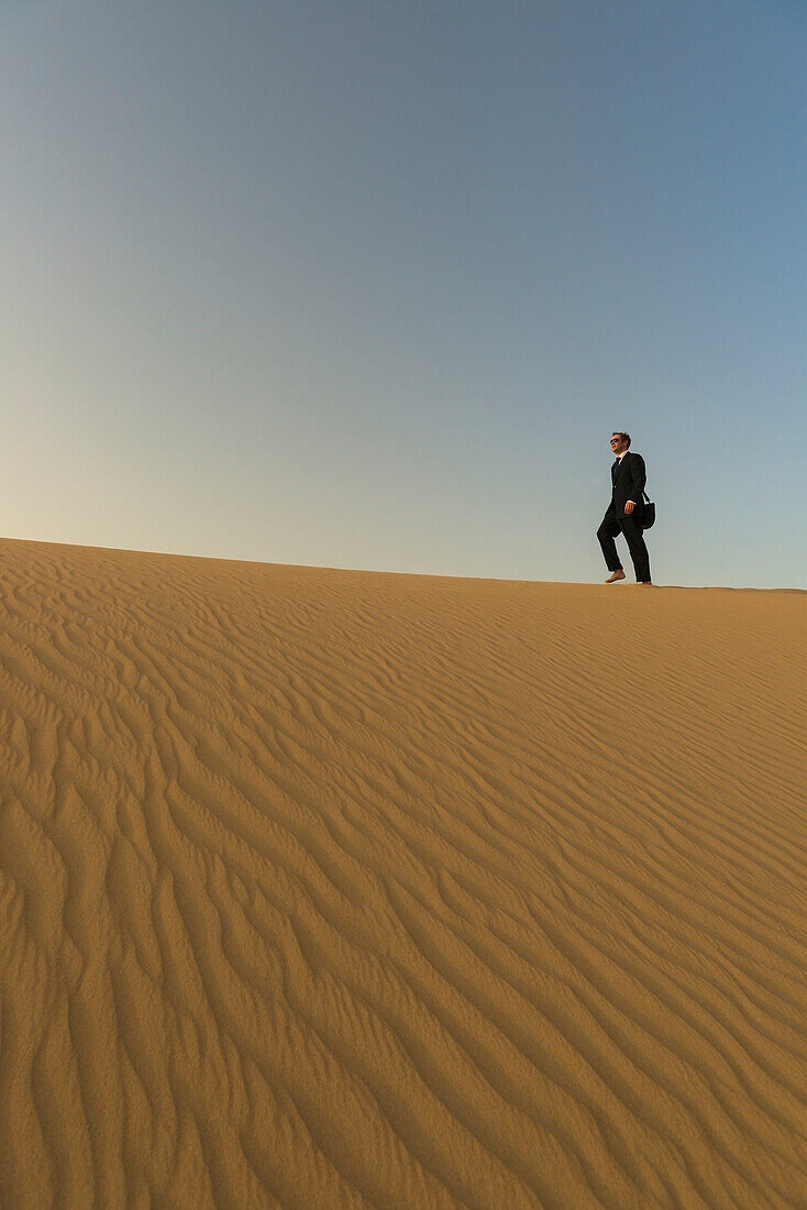 Mann im schicken Anzug, der in der Abenddämmerung auf einer Sanddüne spazieren geht, Dubai, Vereinigte Arabische Emirate