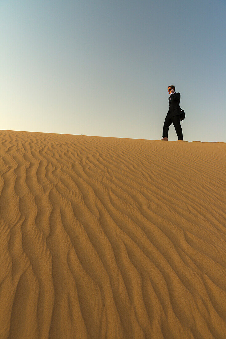 Man In Smart Suit Making Phone Call On Top Of Sand Dune At Dusk,Dubai,United Arab Emirates