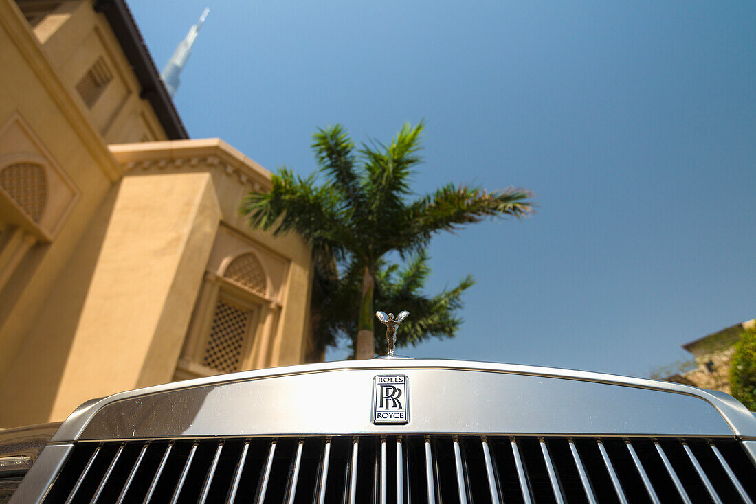 Detail Of Chrome Plated Rolls Royce Beneath Palm Tree And Traditional Arabic Style Hotel With The Burj Khalifa Behind,Dubai,United Arab Emirates