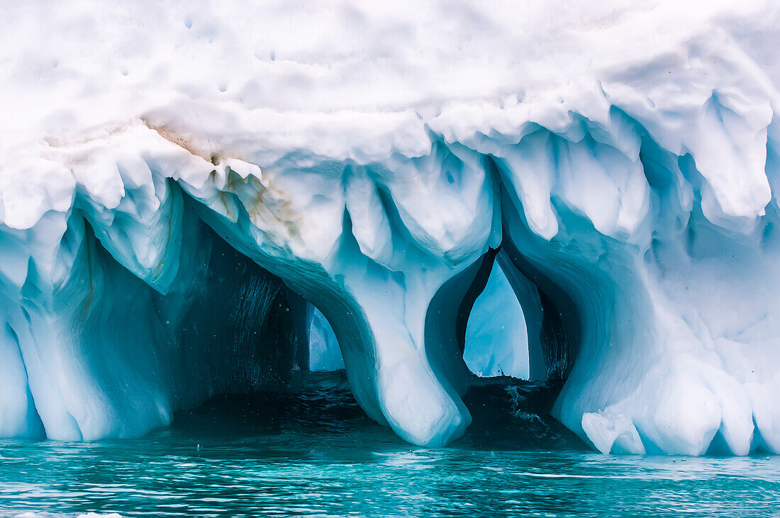 Blue ice tunnels form from an ice formation at the water's edge,Antarctica