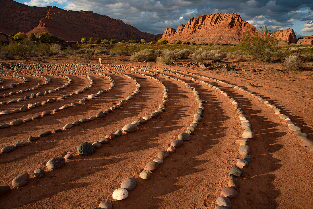 Hiking trail through Snow Canyon,with circles of stones in a meeting area behind the Red Mountain Spa,with meditation maze and Snow Canyon Mountain Range in the background. Red Cliffs Desert Reserve around St George Town with rock cliffs and dark clouds in a blue sky,St George,Utah,United States of America