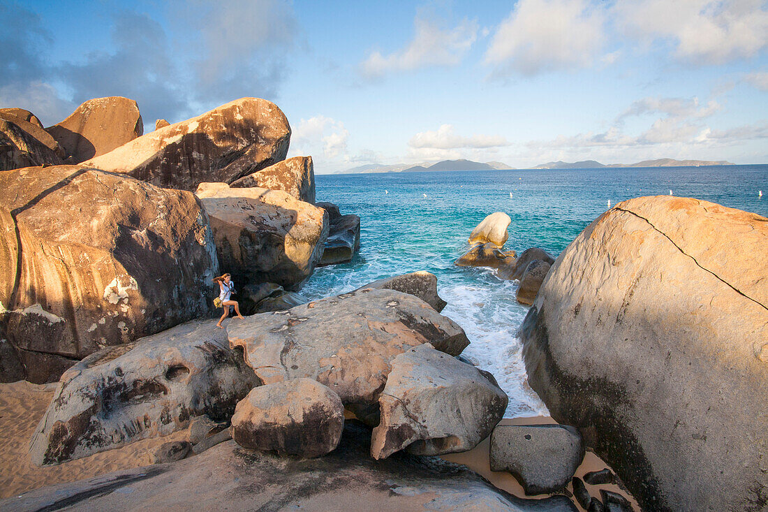 Blick auf eine Frau, die in der Dämmerung auf den großen Felsen am Strand von The Baths spazieren geht, einem berühmten Strand auf den BVI's, Virgin Gorda, British Virgin Islands, Karibik