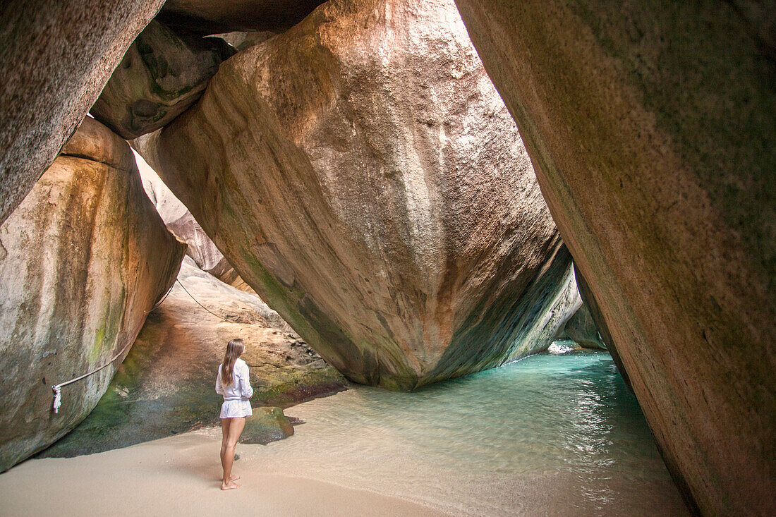 Frau steht unter den großen Felsbrocken an der Küste von The Baths, einem berühmten Strand auf den BVI, Virgin Gorda, British Virgin Islands, Karibik