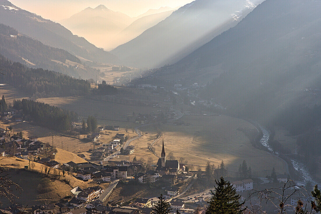 Schleier von Fahrzeugabgasen vernebeln ein Tal in Passeier, was in den Dörfern zwischen den Bergen ein zunehmendes Problem darstellt. Die Luft ist unter den Wolken in den Alpen gefangen, was zu einer Verschmutzung in dieser idyllischen Szene führt, Passeier, Italien