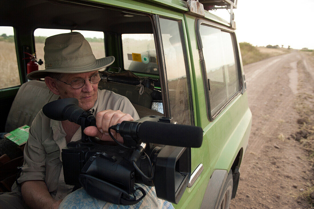 Videofilmer fährt in einem Safari-Geländewagen im Queen Elizabeth National Park, Mweya, Uganda