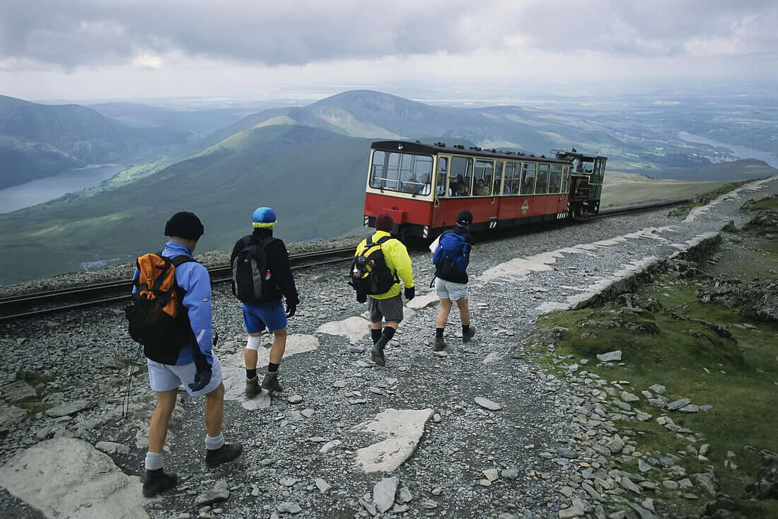 Ein mit Touristen gefüllter Zug passiert Wanderer beim Abstieg vom Mount Snowdon in Wales,Wales