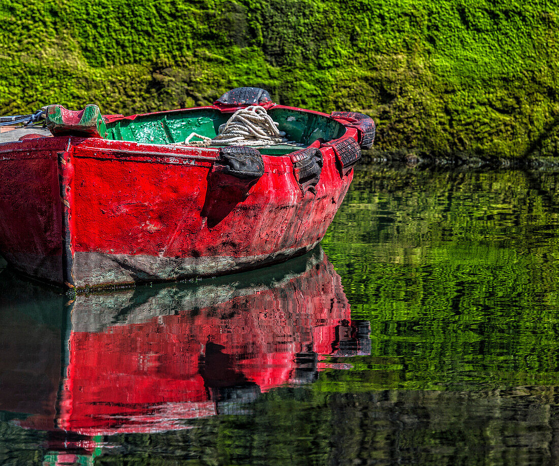 Small,wooden fishing boat moored to the shore with a mirror image reflection in the calm water in the coastal town of Getaria,Getaria,Gipuzkoa,Spain
