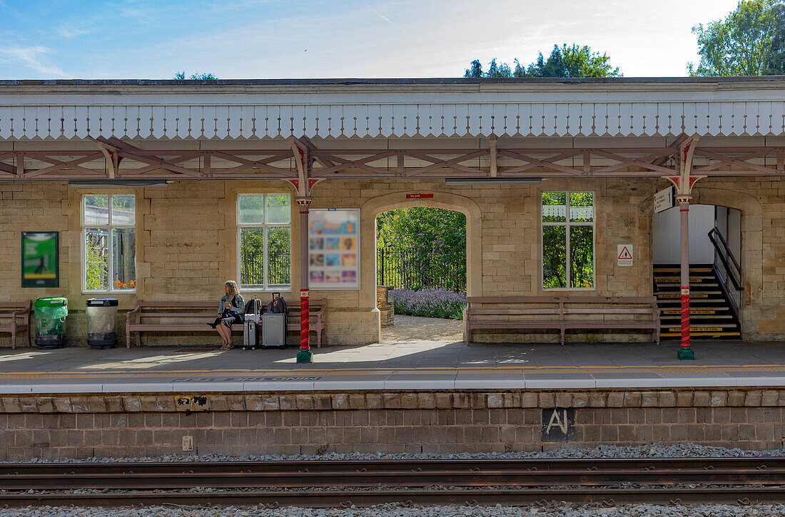 Reife Frau wartet mit Gepäck an einem Bahnhof, Vereinigtes Königreich