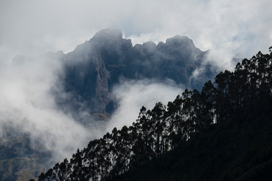Wolken umhüllen die zerklüfteten Berge mit silhouettierten Bäumen, die den Berghang im Vordergrund säumen, vom Heiligen Tal der Inkas aus gesehen, nördlich von Cuzco, Peru