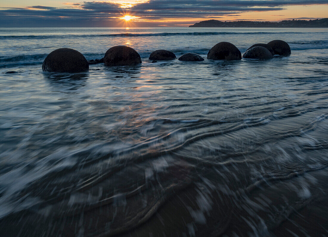 Incoming tide at sunrise with the Moeraki boulders in the surf along a stretch of Koekohe Beach on the South Island of New Zealand,Hampden,North Otago,New Zealand