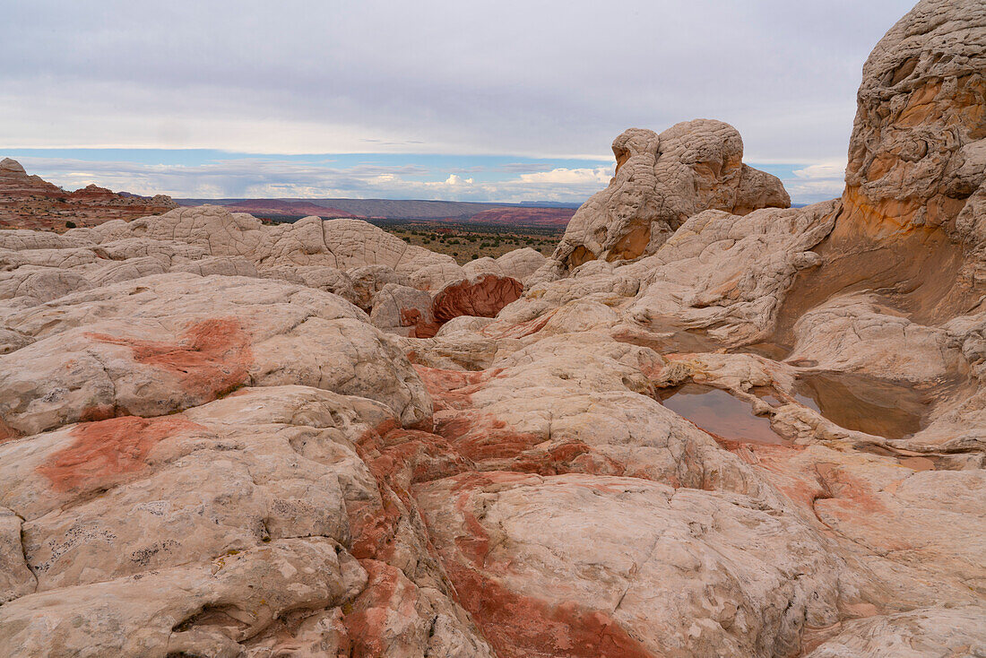 Landschaftliche Ansicht von Felsformationen mit dem Plateau in der Ferne unter einem bewölkten Himmel, die Teil der fremden Landschaft von erstaunlichen Linien, Konturen und Formen in der wundersamen Gegend bekannt als White Pocket, in Arizona, Arizona, Vereinigte Staaten von Amerika
