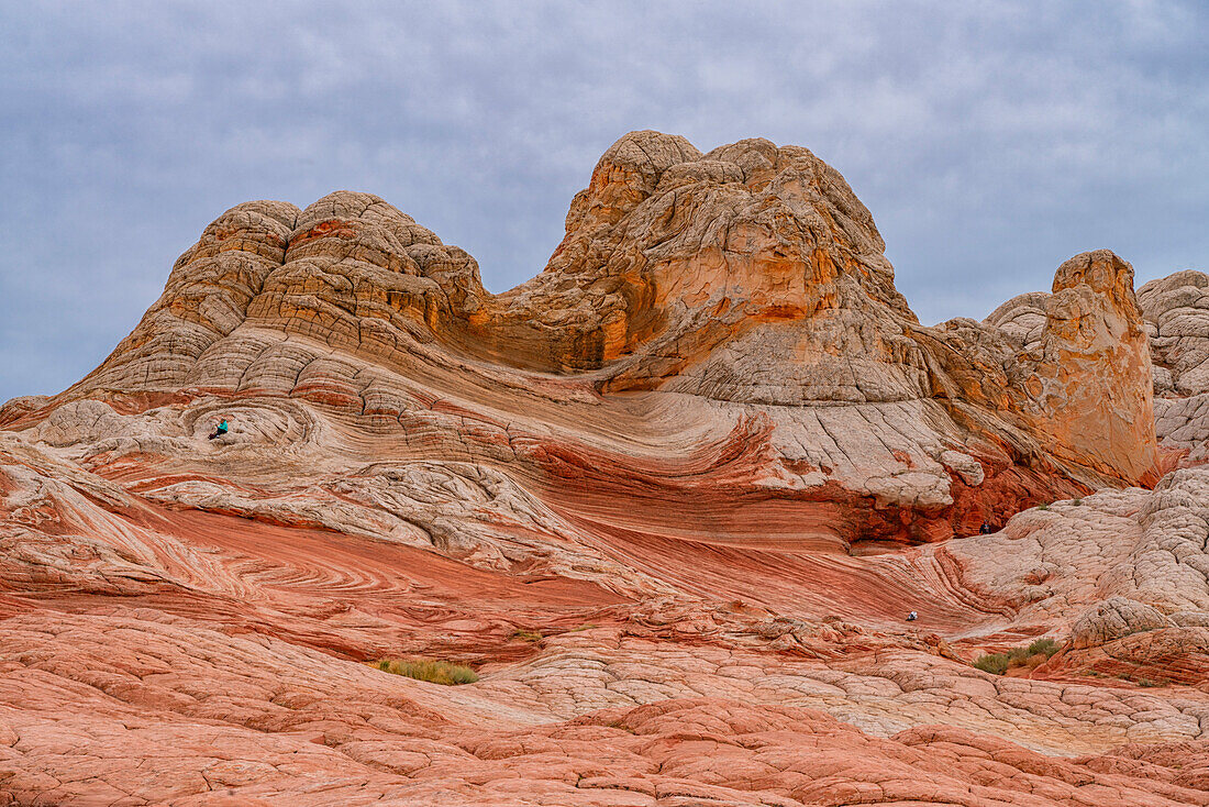 Frau sitzt zwischen den massiven roten Felsformationen unter einem bewölkten Himmel, umgeben von den erodierten Hügeln und erstaunlichen Mustern, die die außerirdischen Landschaften in der wundersamen Gegend von White Rock bilden, Arizona, Vereinigte Staaten von Amerika