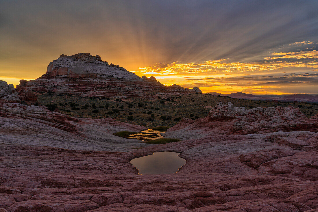 Sonnenuntergang mit dämmrigen Strahlen über dem wundersamen Gebiet, das als White Pocket bekannt ist und in Arizona liegt. Es ist eine fremde Landschaft mit erstaunlichen Linien, Konturen und Formen. Hier erzeugt die untergehende Sonne wunderschöne Farben am Himmel über dem Gebiet, Arizona, Vereinigte Staaten von Amerika