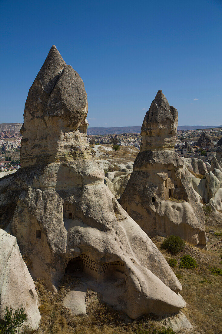 Cave Houses carved into the volcanic rock formations called Fairy Chimneys,against a bright blue sky near the town of Goreme in the background in Pigeon Valley,Cappadocia Region,Nevsehir Province,Turkey