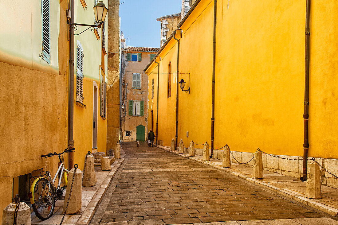 Mann und Hund auf einer Straße zwischen gelben Gebäuden, Saint-Tropez, Frankreich