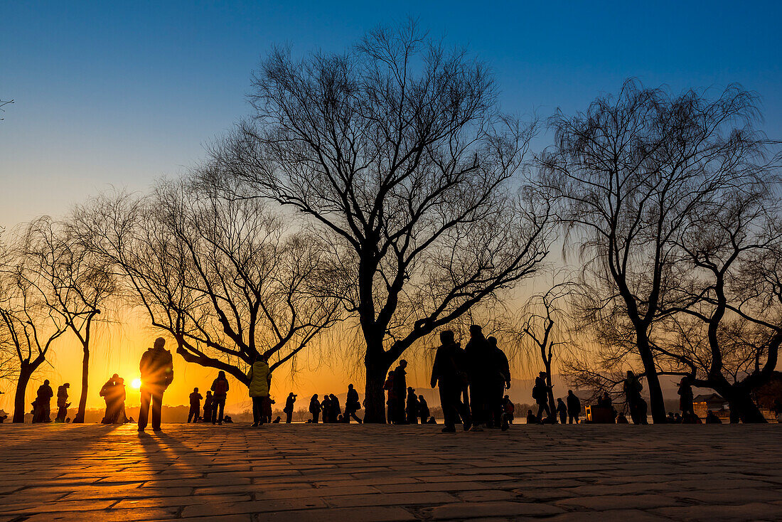 Silhouetten von Bäumen und Touristen bei Sonnenuntergang, Der Sommerpalast, Peking, China