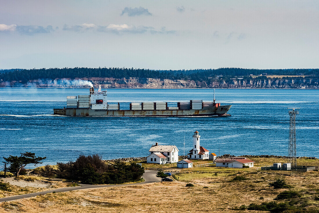 Frachtschiff, das von der Straße von Juan de Fuca über die Admiralty Bucht in den Puget Sound einfährt. Der Point Wilson Lighthouse befindet sich im Fort Worden Historical State Park in der Nähe der Stadt Port Townsend. Im Hintergrund ist Whidbey Island zu sehen,Washington,Vereinigte Staaten von Amerika