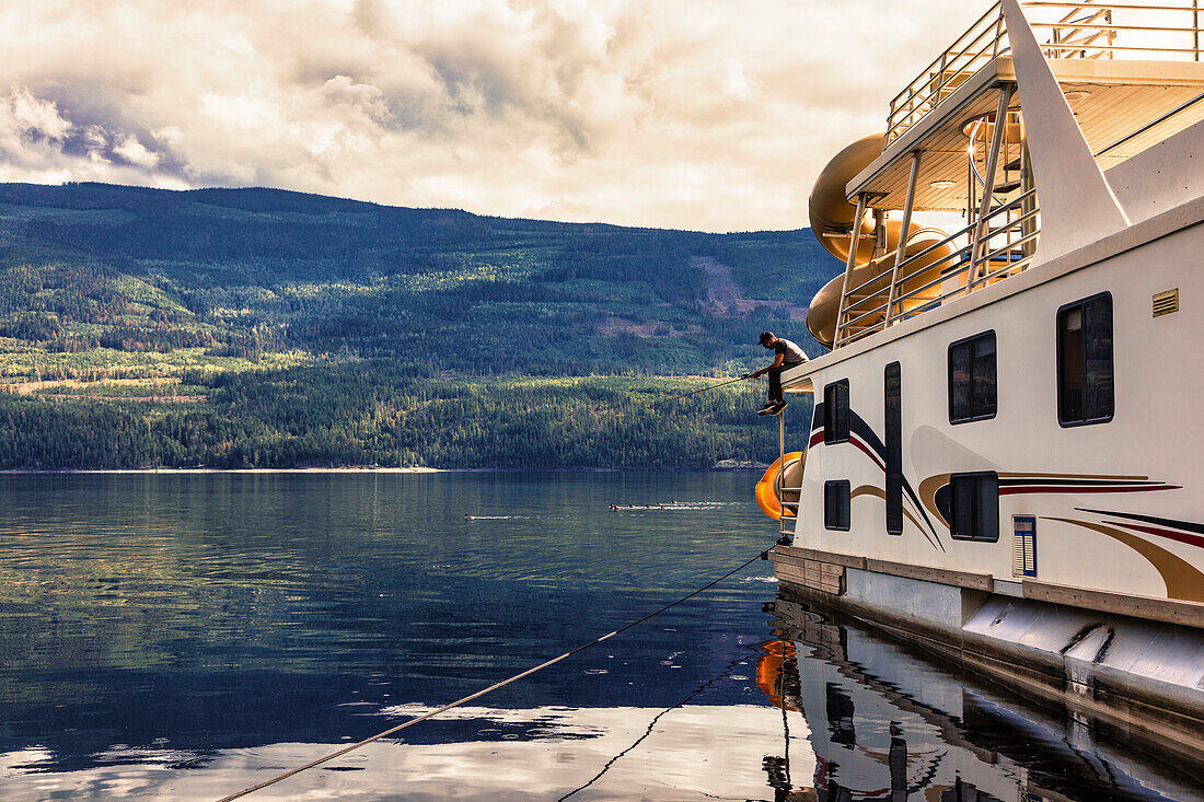 Mann genießt einen Familienurlaub auf einem Hausboot und angelt vom Deck des Hausboots, während es am Ufer des Shuswap Lake, Shuswap Lake, British Columbia, Kanada, geparkt ist