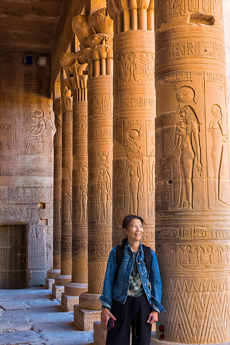 A female Chinese tourist stands among a row of columns with ancient Egyptian hieroglyphic details at the Philae Temple,Aswan,Egypt,Africa