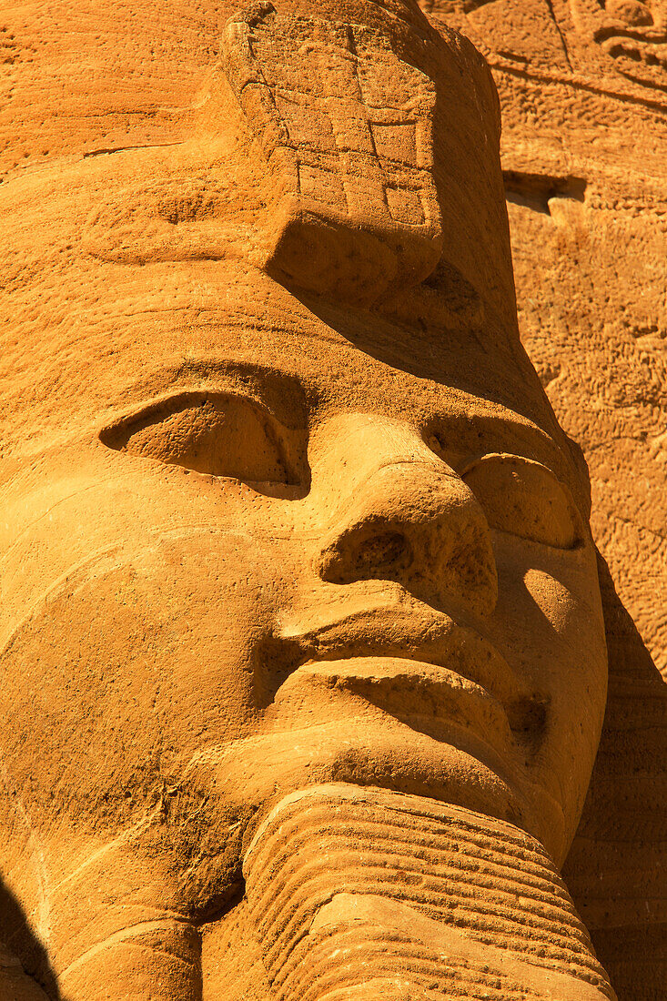 Nahaufnahme einer der in den Berghang gehauenen Statuen von Ramses II. an der Vorderseite des Großen Sonnentempels von Abu Simbel mit goldenem Licht, Abu Simbel, Nubien, Ägypten