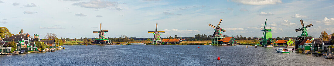 Panorama of historical wooden windmills along a riverbank with blue sky and clouds,Zaandam,Netherlands