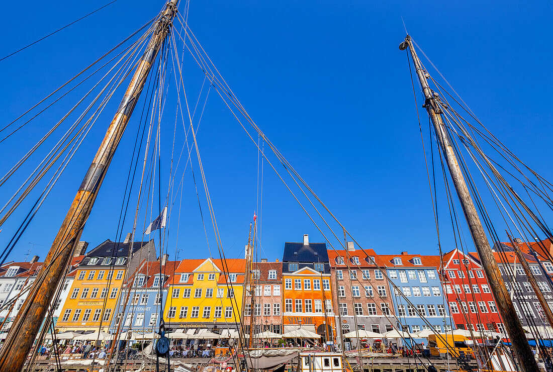 Boats and people along a colourful waterfront called Nyhavn,viewed through the boat masts,Copenhagen,Denmark