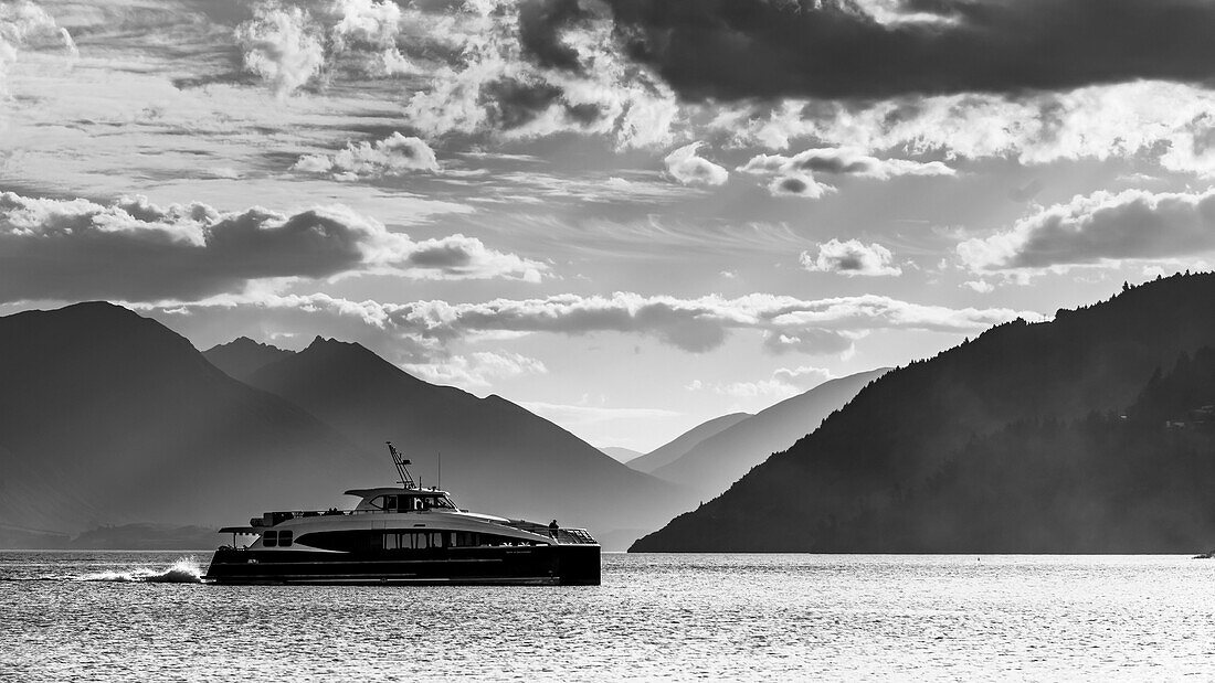 Yacht auf dem Lake Wakatipu mit dramatischer Beleuchtung und Silhouetten der Berge im Hintergrund, Queenstown, Südinsel, Neuseeland