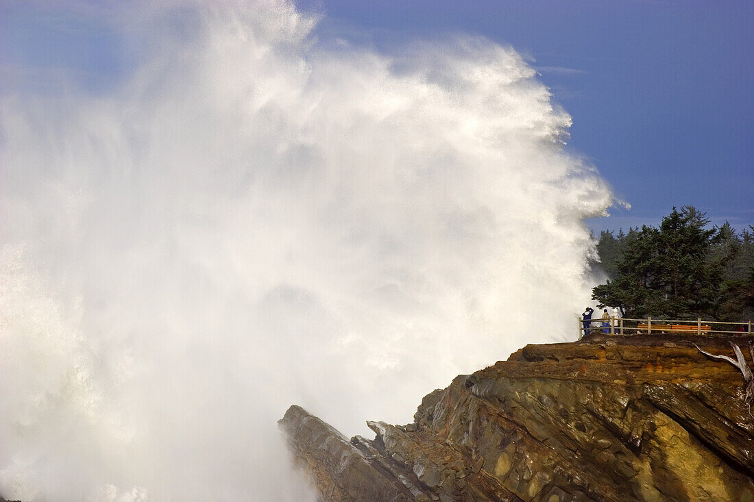 Mächtige Welle, die sich an den Felsen im Shore Acres State Park bricht, während Touristen an einem Aussichtspunkt stehen und das heftige Platschen beobachten und nass werden, Küste von Oregon, Oregon, Vereinigte Staaten von Amerika