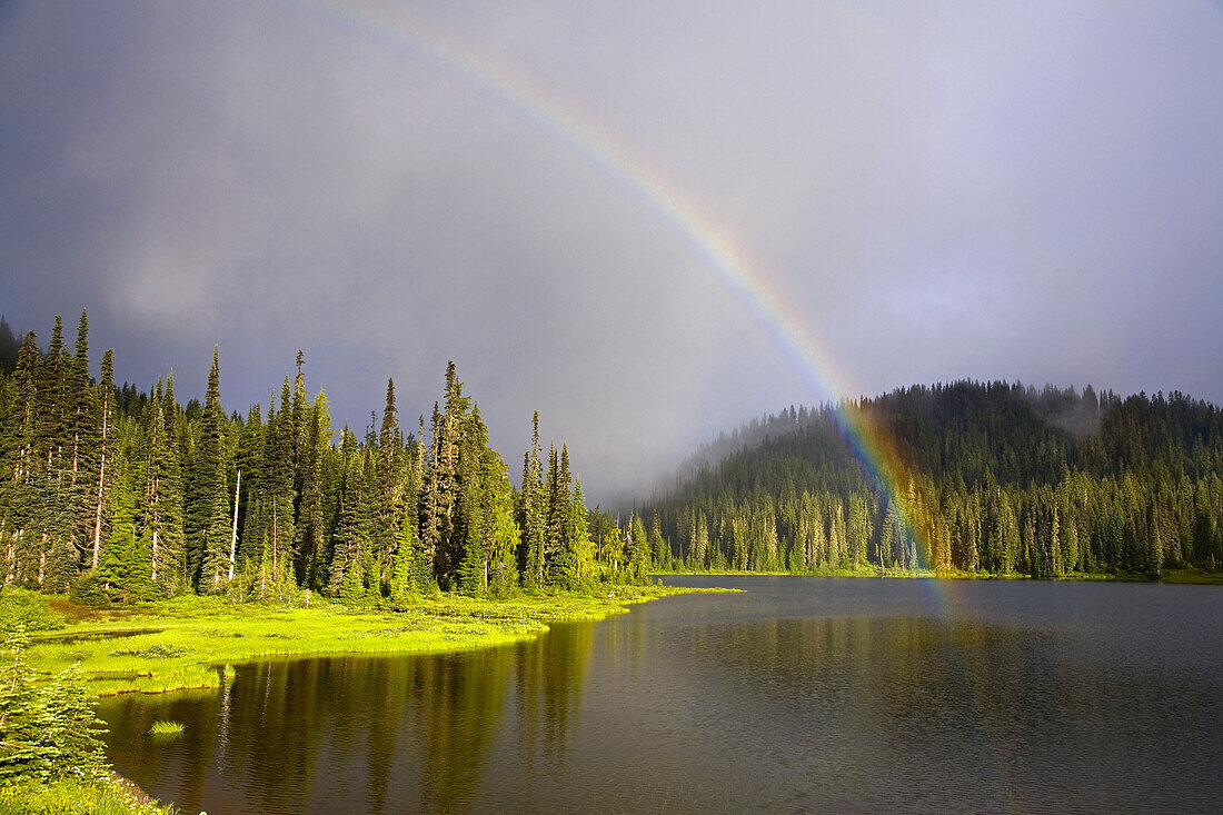 Regenbogen, der sich nach einem Gewitter von den Gewitterwolken zu einem ruhigen See spannt, Mount Rainier National Park, Washington, Vereinigte Staaten von Amerika