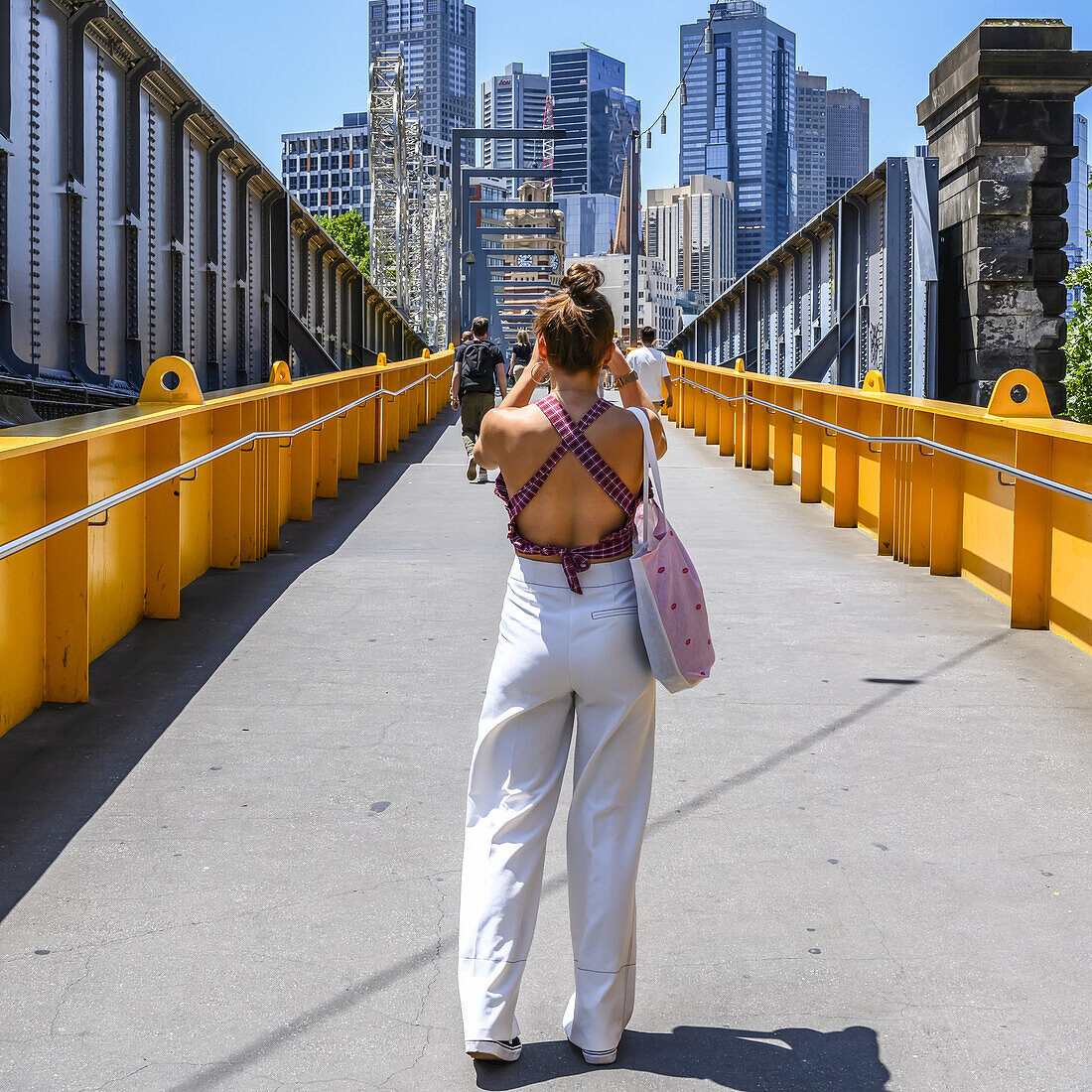 Blick von hinten auf eine Touristin, die die Skyline von Melbourne von einer Fußgängerbrücke aus fotografiert, Melbourne, Victoria, Australien