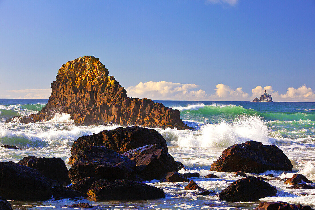 Tillamook Rock Light,a deactivated lighthouse off the coast of Oregon,seen in the distance and waves of the surf rolling into shore and splashing into rocks,Oregon,United States of America