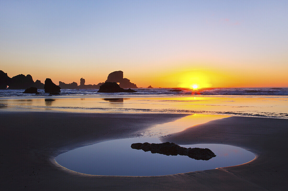Helle untergehende Sonne, die unter dem Horizont über dem Wasser mit Felsformationen entlang der Küste von Oregon untergeht,Oregon,Vereinigte Staaten von Amerika