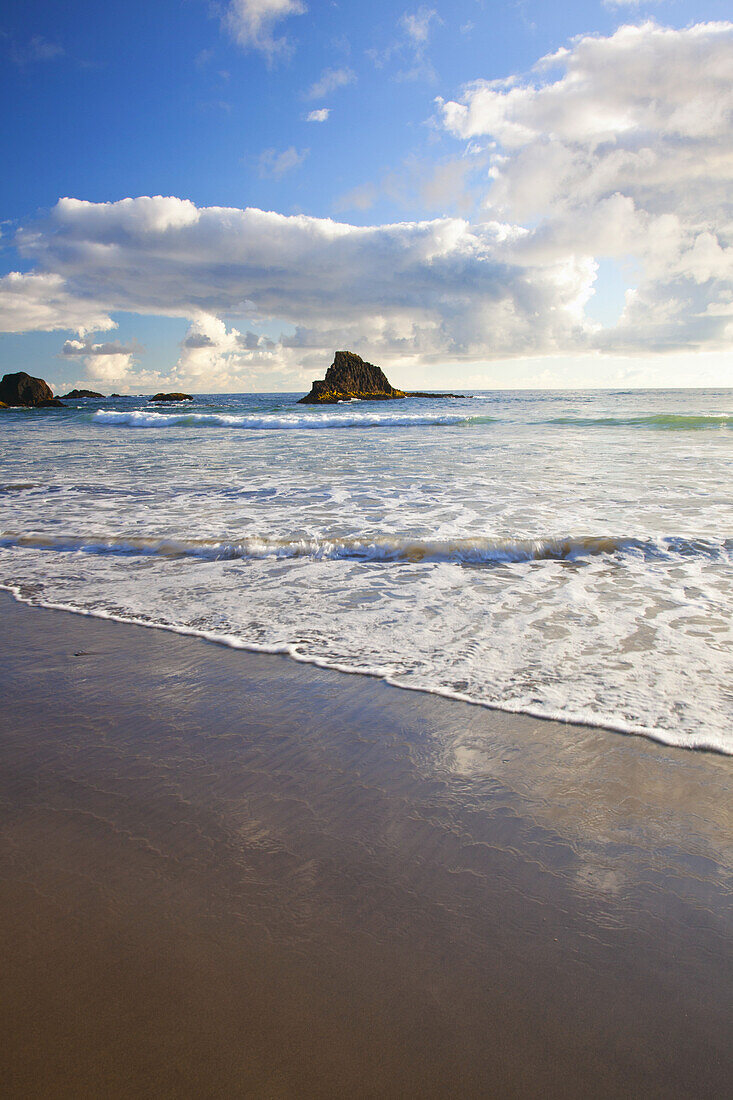 Ruhige Szene an der Küste von Oregon mit einer sanften Brandung, die an den Strand gespült wird, und Felsformationen entlang der Küste, Oregon, Vereinigte Staaten von Amerika