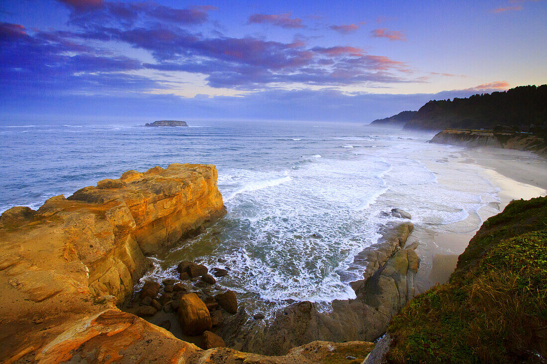 Zerklüftete Klippen entlang der Küste von Oregon mit Nebel, der von der Brandung aufsteigt und bei Sonnenaufgang an den Strand gespült wird, Oregon, Vereinigte Staaten von Amerika