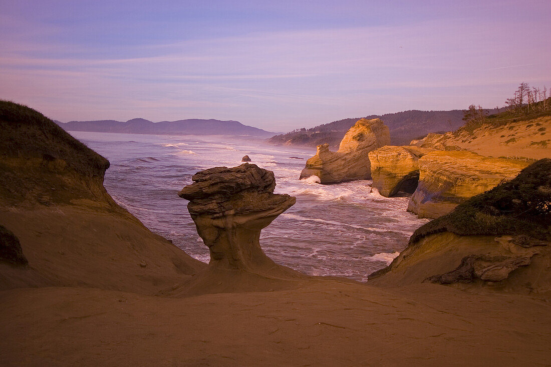 Zerklüftete Küstenlinie mit Klippen und Felsformationen und die Brandung, die bei Sonnenuntergang an das Ufer gespült wird, Oregon, Vereinigte Staaten von Amerika