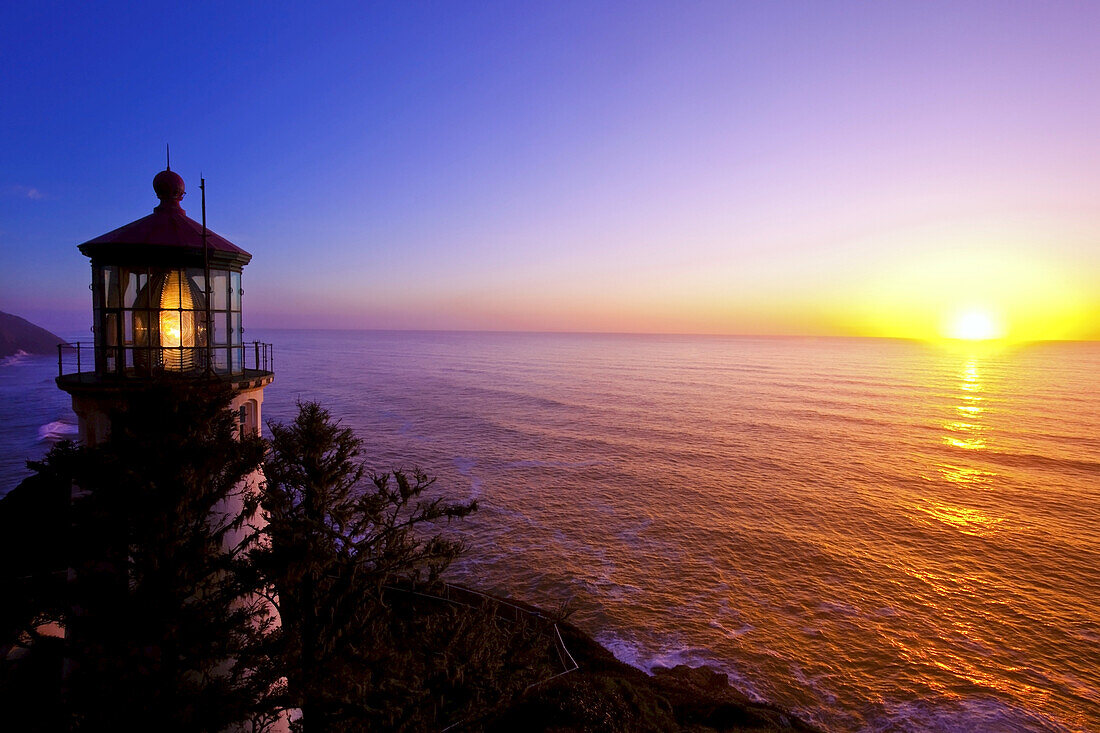 Heceta Head Light bei Sonnenaufgang mit der hellen Sonne, die über dem ruhigen Pazifischen Ozean aufgeht und bunte Reflexe auf das Wasser wirft, Pazifischer Nordwesten, Oregon, Vereinigte Staaten von Amerika