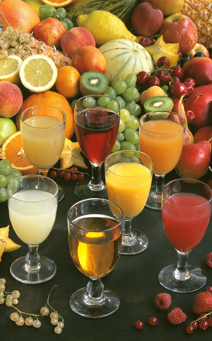 Seven different fruit juices in front of fresh fruit