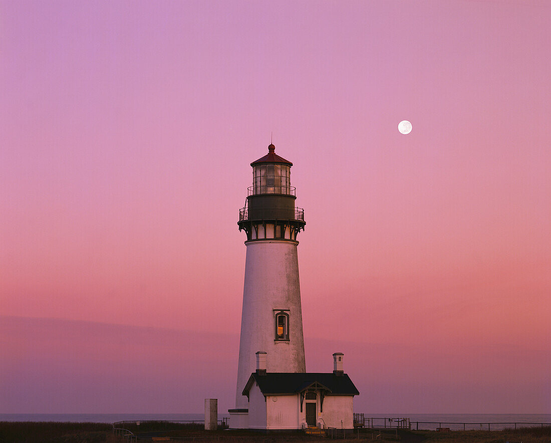 Yaquina Head Light against a glowing pink sunset sky with full moon,Oregon,United States of America