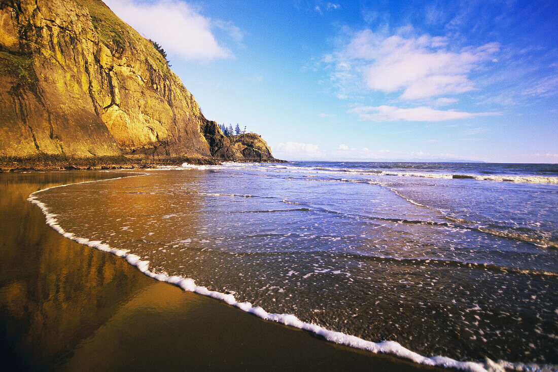 Brandung, die an den Strand entlang der Küste Washingtons gespült wird, mit dem Cape Disappointment Lighthouse in der Ferne, Washington, Vereinigte Staaten von Amerika