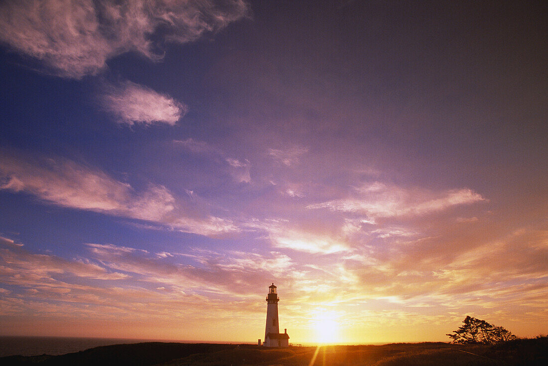 Yaquina Head Light backlit by a bright sun setting over the pacific ocean viewed from Yaquina Bay State Park,Oregon,United States of America