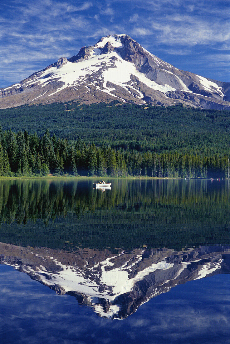 Sitzen in einem kleinen Ruderboot auf dem ruhigen Wasser des Trillium Lake mit einem Spiegelbild des Mount Hood und des Mount Hood National Forest, der sich im Wasser spiegelt, Oregon, Vereinigte Staaten von Amerika