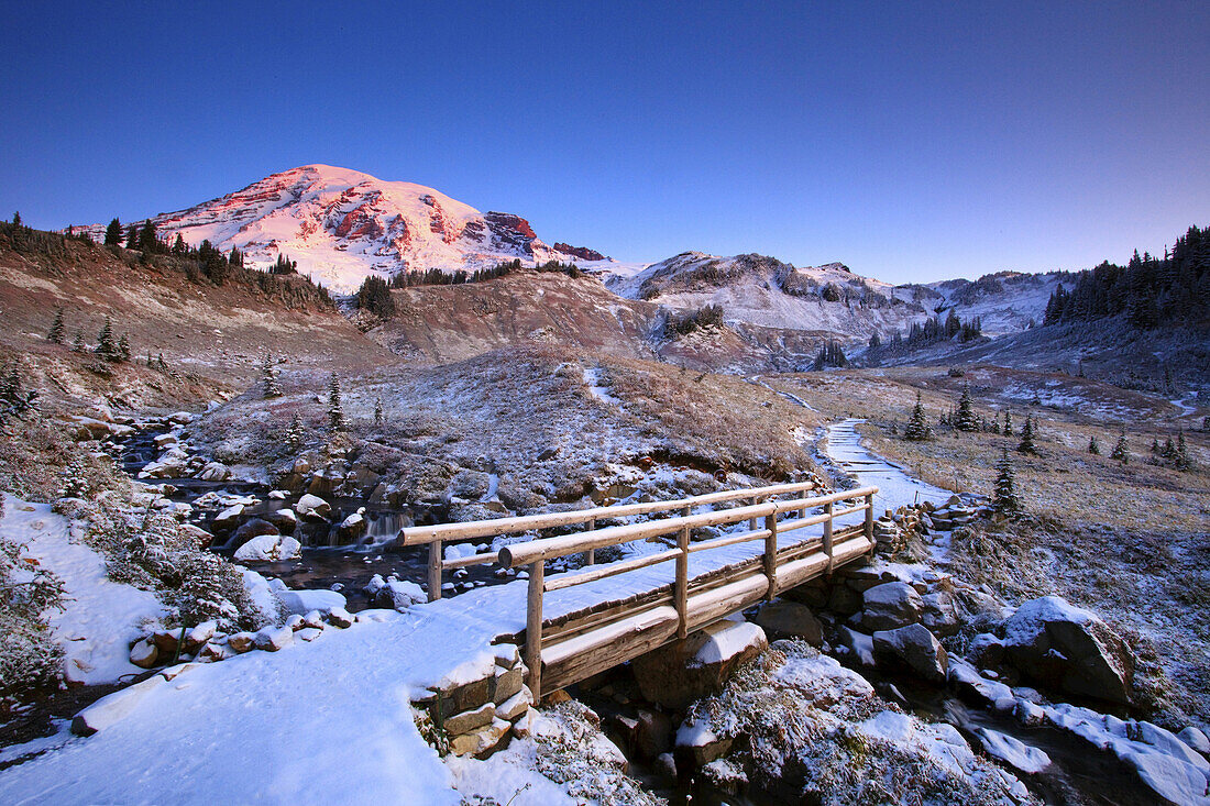Bridge and trail through the Cascade Mountains in winter,with snow-covered Mount Rainier and Edith Creek in Paradise Park,Mount Rainier National Park,Washington,United States of America