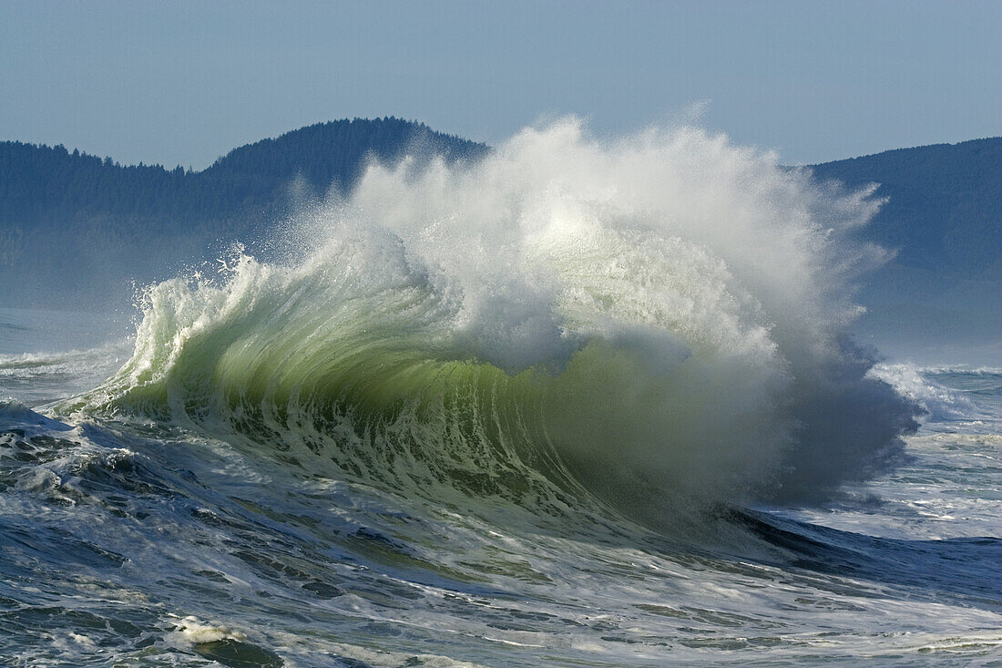 Spritzende Welle, die sich am Ufer bricht, mit der Küstenlinie von Oregon im Hintergrund am Cape Kiwanda, Pacific City, Oregon, Vereinigte Staaten von Amerika
