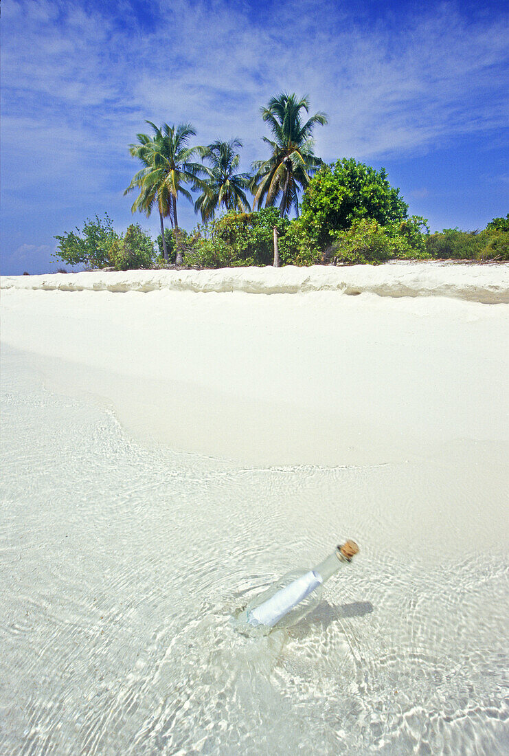 Flaschenpost, eine klare Glasflasche mit einer Papiernotiz schwimmt im klaren türkisfarbenen Wasser des Indischen Ozeans mit einem weißen Sandstrand im Hintergrund, Malediven