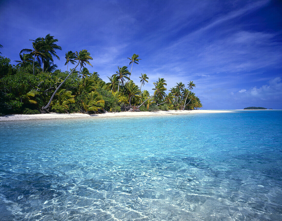 Palm trees line the white sand beach of an island with clear turquoise water and bright blue sky,Cook Islands