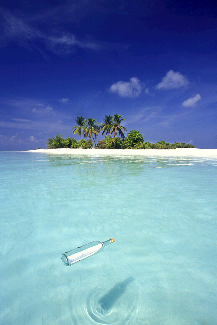 Flaschenpost, eine klare Glasflasche mit einer Papiernotiz schwimmt im klaren türkisfarbenen Wasser des Indischen Ozeans mit einem weißen Sandstrand im Hintergrund, Malediven