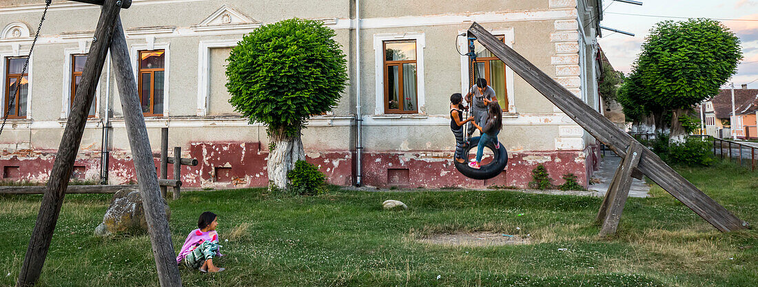 Einheimische Kinder spielen auf einer Reifenschaukel auf einem Dorfspielplatz, Siebenbürgen, Dacia, Kreis Brasov, Rumänien