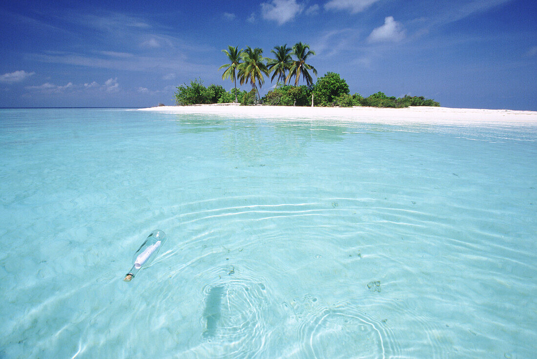 Message in a bottle,a clear glass bottle with a paper note floats in the clear turquoise water of the Indian Ocean with a white sand beach in the background,Maldives